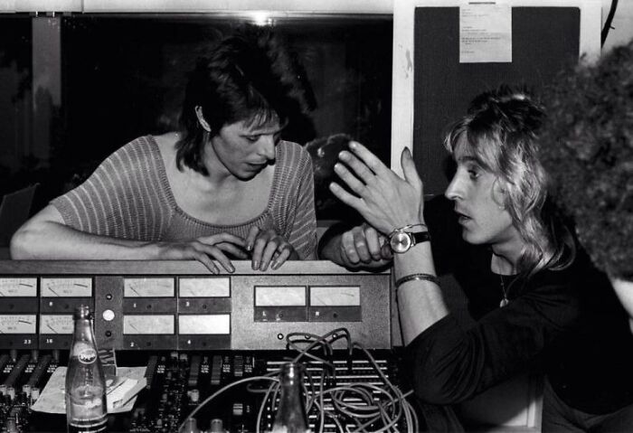 1970s rock legends collaborating in a recording studio surrounded by vintage audio equipment and instruments.