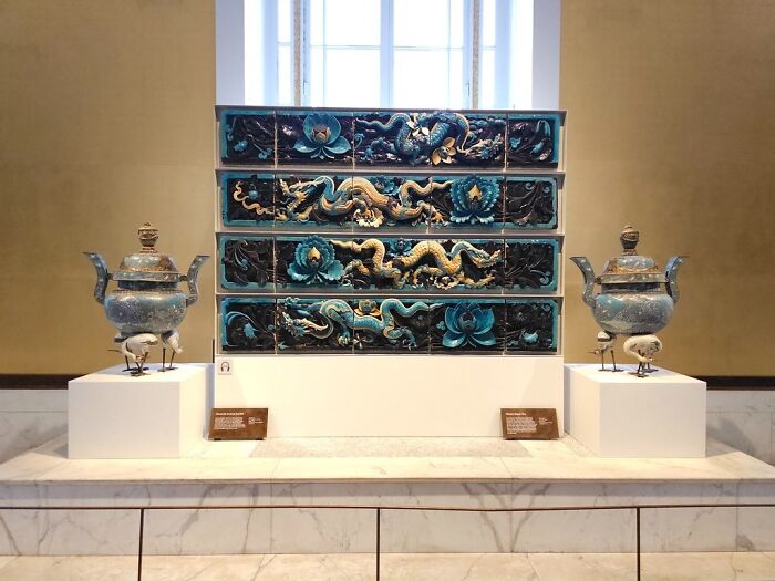 Intricately carved foreign artifacts with dragon motifs displayed at the British Museum on white pedestals and marble surface.