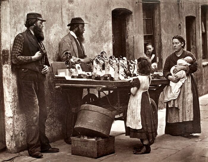 Street scene depicting how London's poorest lived in the 1800s with a family and street vendors outside a building.