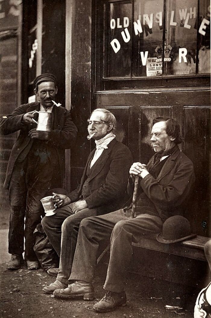 Three men smoking pipes outside a London pub, representing how London's poorest really lived in the 1800s.
