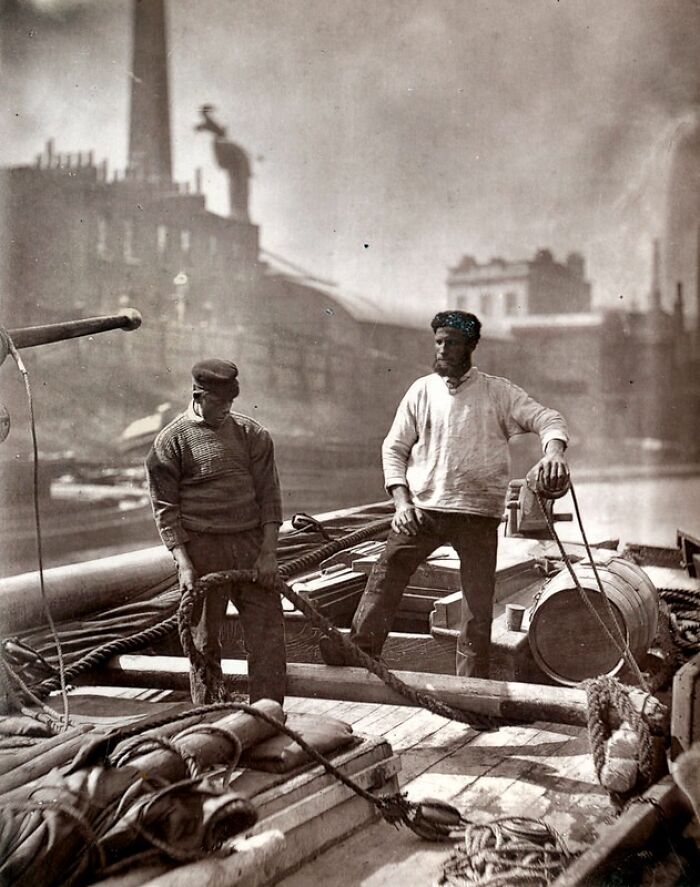 Two working-class men on a dock in 1800s London, showing how London's poorest really lived with industrial buildings behind.