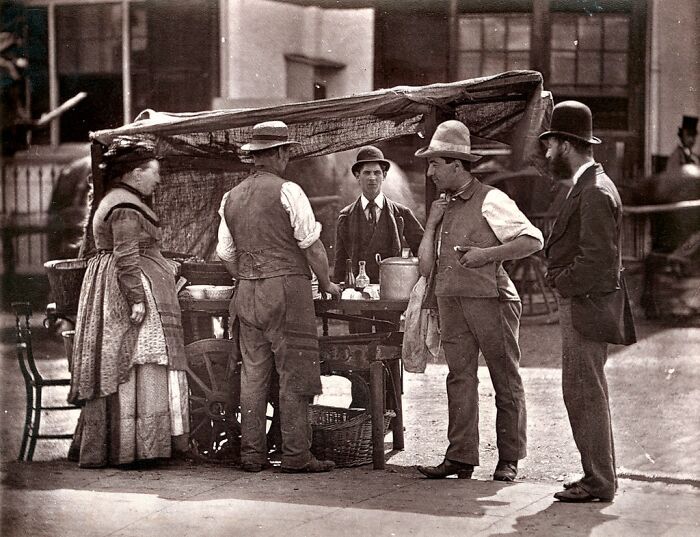 London's poorest people gathered around a street vendor cart, showing daily life in the 1800s.