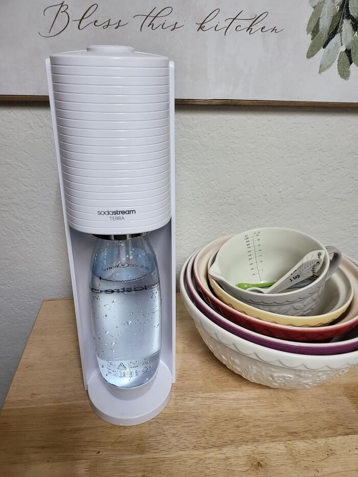 Sodastream Terra sparkling water maker next to stacked ceramic mixing bowls with measuring spoons on a kitchen counter.