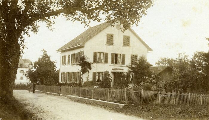 Vintage historical photograph showing a residential street scene with houses and trees from 100 years ago.