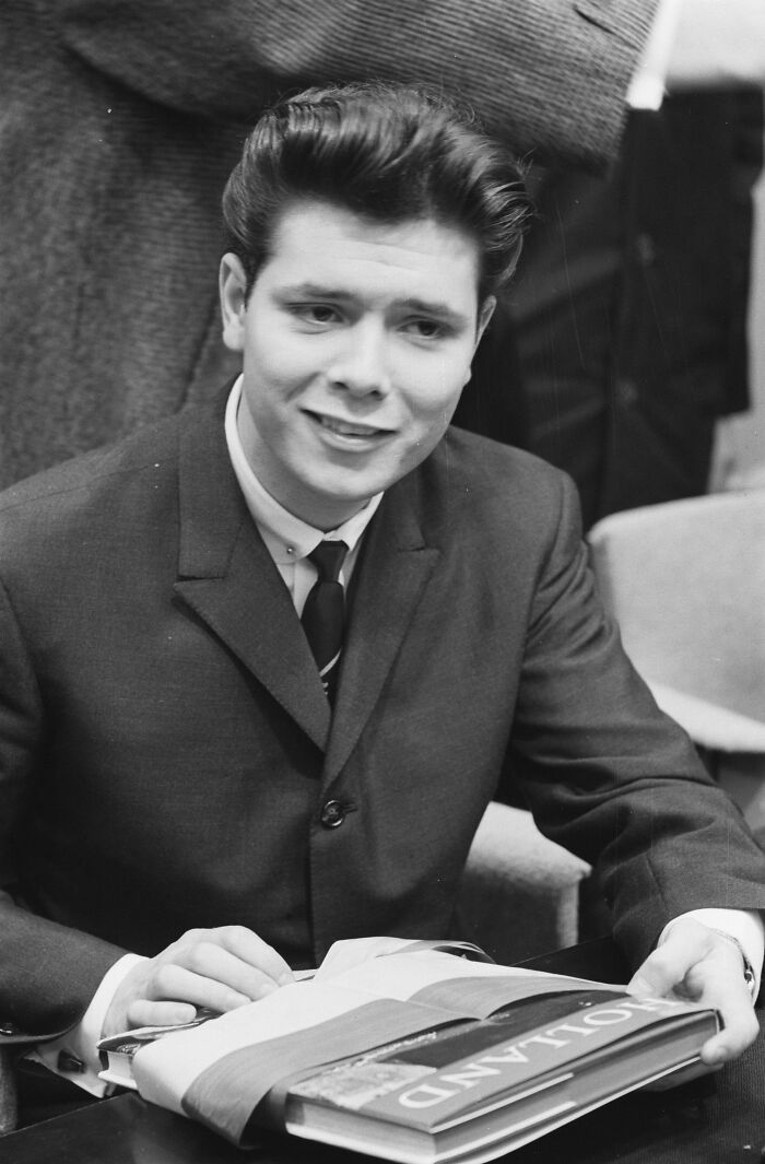 Young man in a classic 20th century Teddy Boy suit smiling while holding a book, embodying Teddy Boy era style.