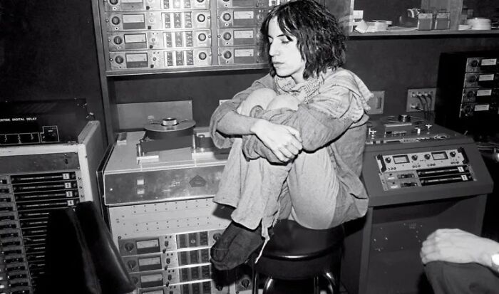 1970s rock legend in a recording studio surrounded by vintage audio equipment during music creation session.