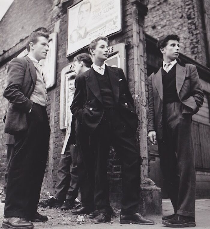 Group of young men dressed in classic 20th century Teddy Boy era fashion standing on a street corner.
