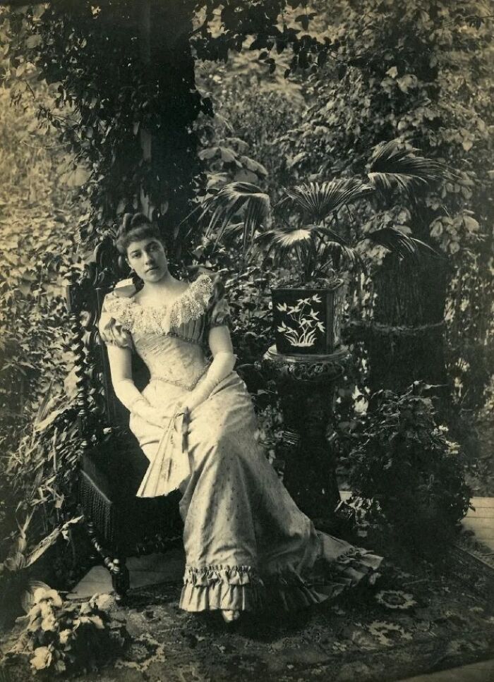 Vintage portrait of a woman in an elegant 1900s dress seated among lush plants, showcasing the beauty of women from the 1900s.