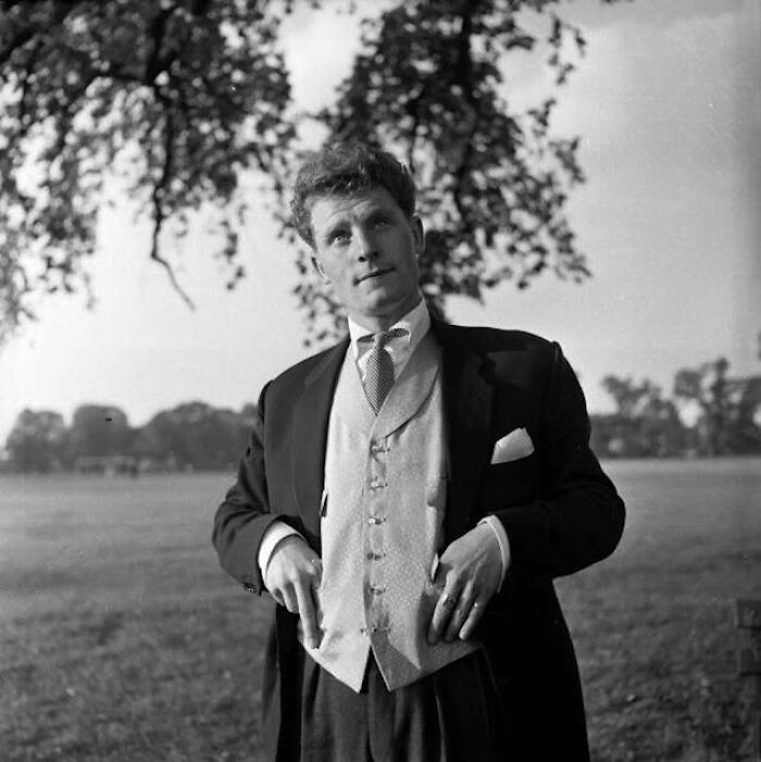 Black and white photo of a man dressed in classic 20th century Teddy Boy era style outdoors under a tree.