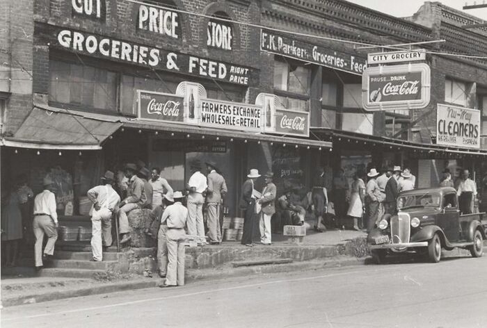 People gathered outside a grocery store during the Great Depression era in a rare historical black and white photo.