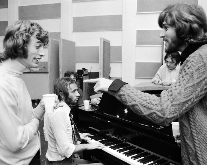 1970s rock legends in a studio session playing piano and discussing music creation in a casual recording environment.