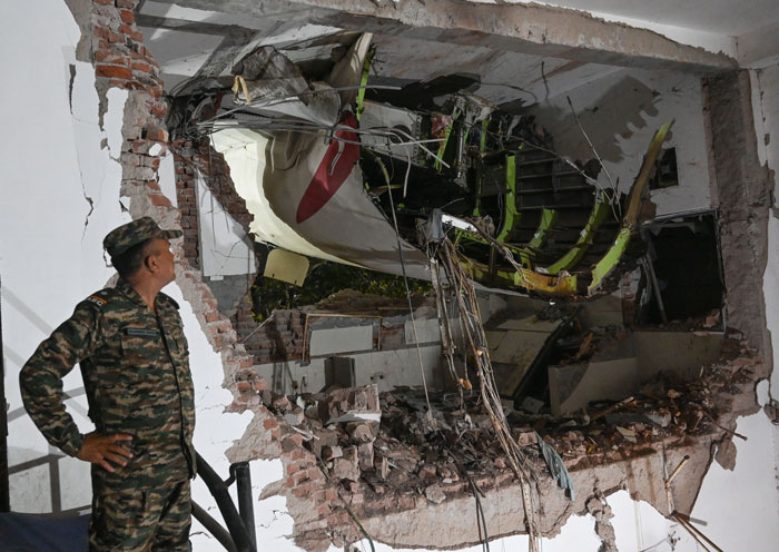Air India pilot’s plane crash site with security guard inspecting damaged building wreckage at night. - 4