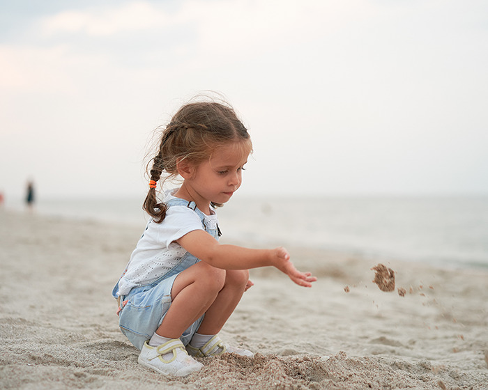 Young girl playing with sand on the beach during staged momfluencer pretend life photo session for online fame. - 3