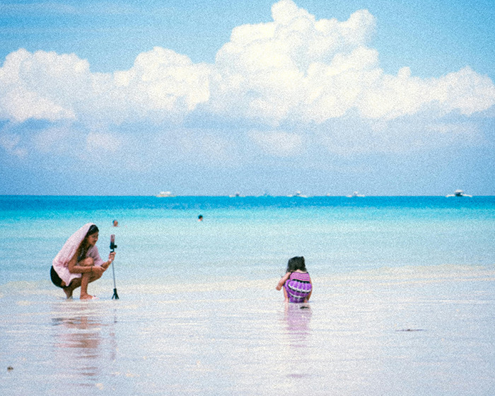 Momfluencer staging a beach day with daughter for online fame, capturing photos by the ocean under blue sky. - 7