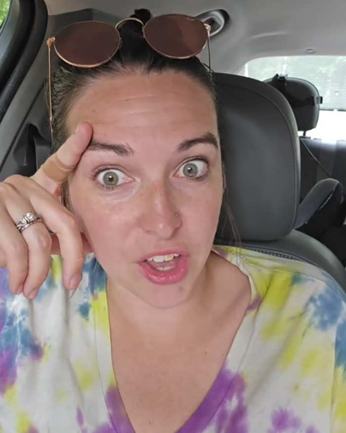 Momfluencer in a car wearing sunglasses on head and a tie-dye shirt, reacting to backlash for staging a beach day with daughter. - 1