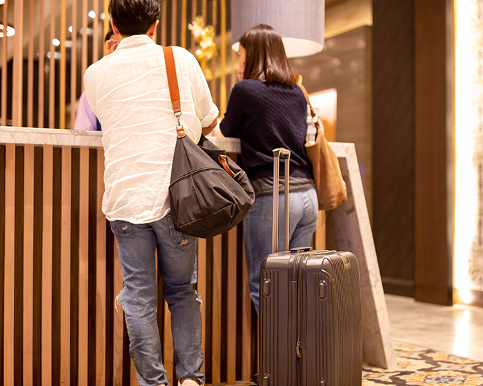 Two travelers at hotel check-in with luggage and bags, illustrating influencer travel hack avoiding luggage fees.