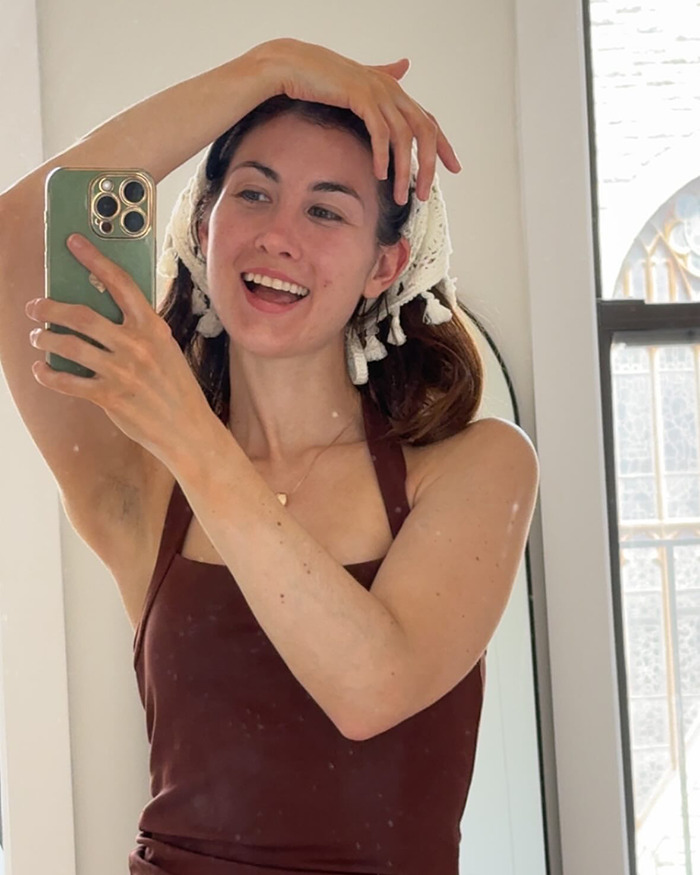 Young woman taking a mirror selfie indoors, smiling while showcasing influencer travel hack and avoiding luggage fees.
