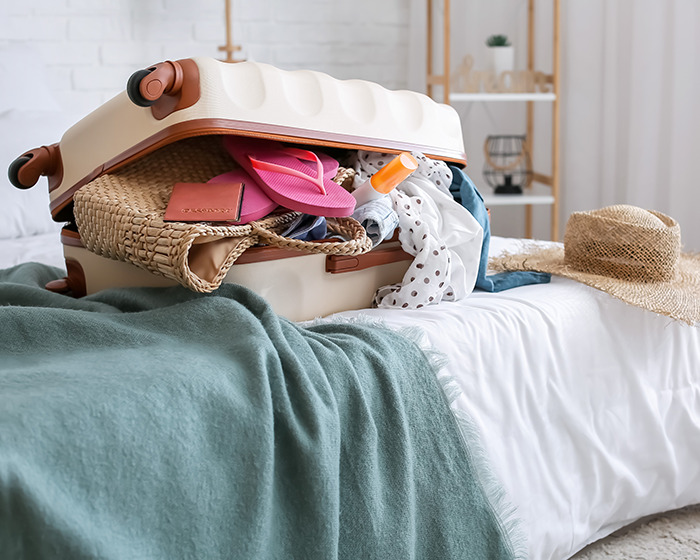 Overpacked suitcase on bed with clothes and travel items spilling out, illustrating influencer's travel hack backfire.