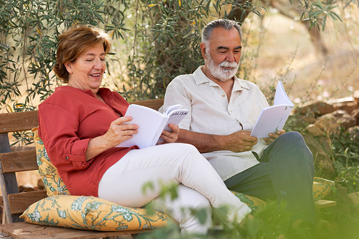 Older couple sitting on a bench outdoors, reading documents and discussing genetic heritage information with smiles. - 1