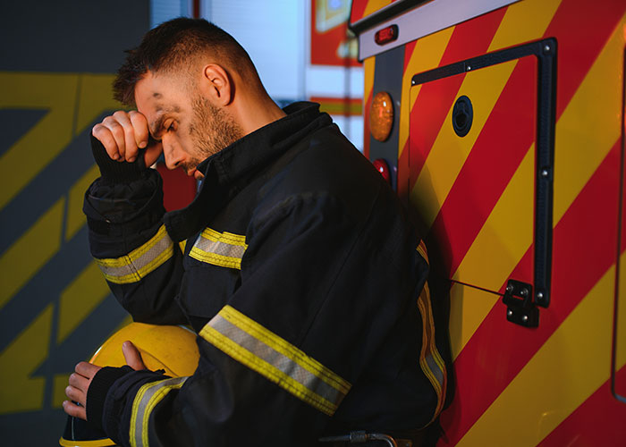 Worried firefighter in uniform holding helmet, leaning against emergency vehicle reflecting creepy true stories haunting people.