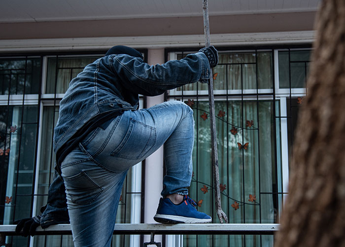 Person wearing denim and a mask creeping through a window, depicting a creepy true story that haunts people.