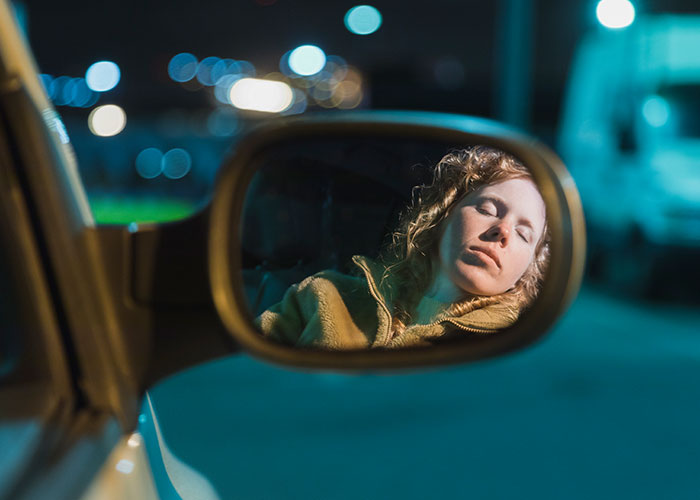 Woman with eyes closed reflected in car mirror at night, creating a creepy true story atmosphere that haunts people.