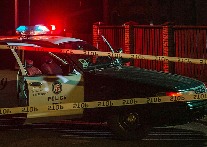 Police car with flashing lights behind yellow crime scene tape at night, related to creepy true stories that haunt people.
