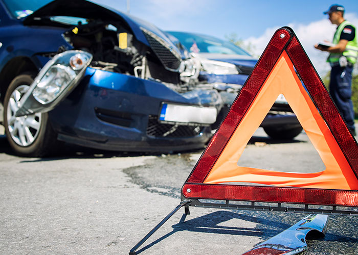 Warning triangle on road after a car accident with damaged front and police officer nearby, creepy true stories concept.