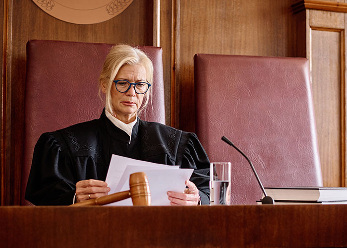 Female judge reading documents at courtroom bench with gavel and glass of water related to creepy true stories.