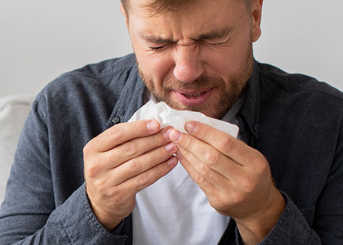 Man with closed eyes holding tissue to his nose, appearing uncomfortable, related to creepy true stories that haunt people.