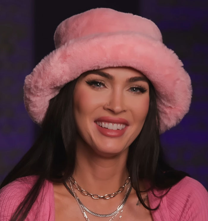 Woman wearing a pink fluffy hat and layered necklaces sharing favorite and awkward encounters with celebrities on camera. - 9