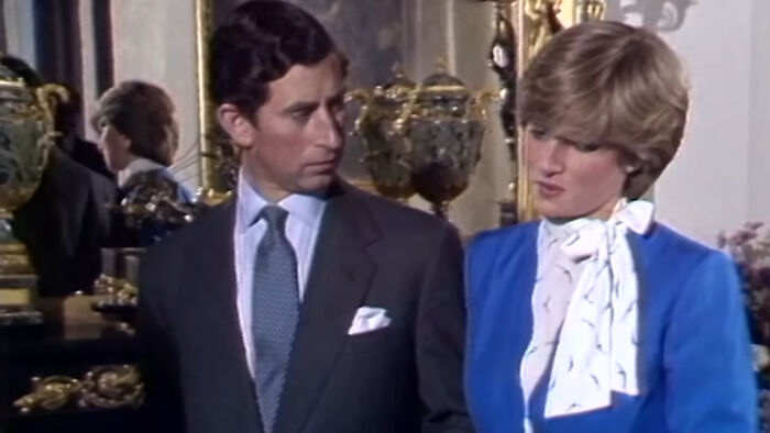 Prince Charles and Princess Diana engaged in a formal conversation indoors with ornate decor in the background, Singapore mass panic topic.