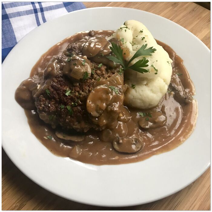 Plate of Salisbury steak covered in mushroom gravy served with mashed potatoes garnished with parsley