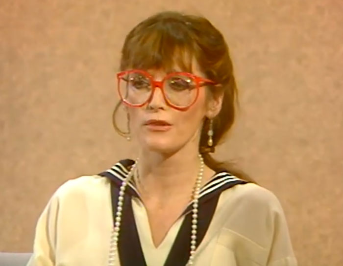 Woman with red glasses and pearl necklace speaking, illustrating incredibly cool facts about the world this June.