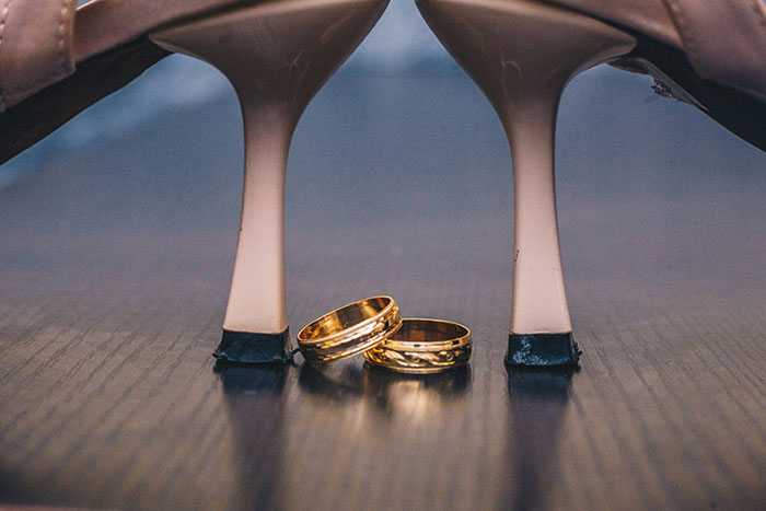 Close-up of two gold rings placed between beige high heels on a reflective wooden surface for world facts.