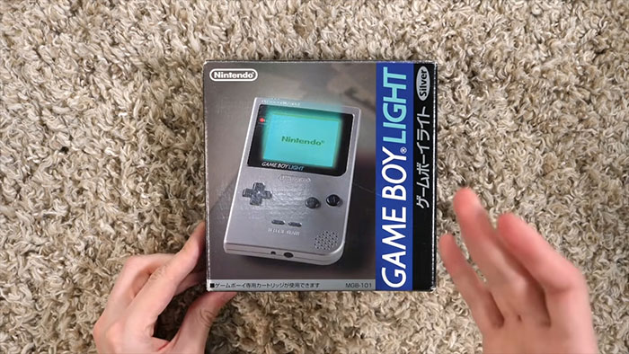 Hands holding a boxed Nintendo Game Boy Light Silver on a carpet, illustrating cool facts about the world.