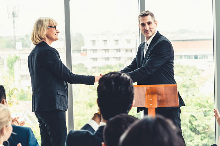 Two professionals shaking hands in an office setting during a presentation about cool facts about the world.