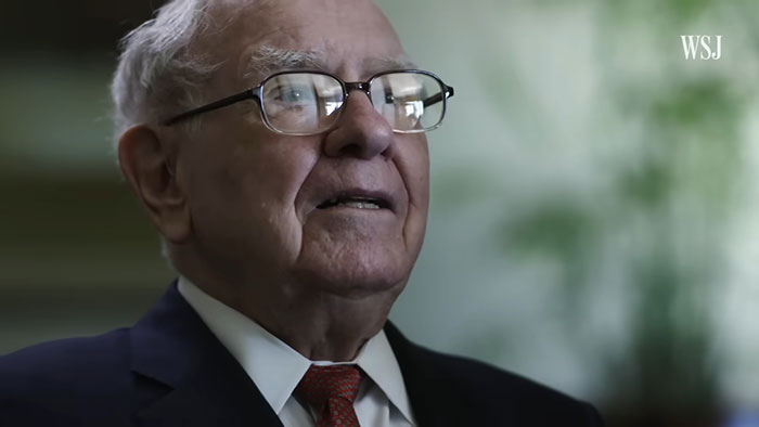 Elderly man wearing glasses and a suit sharing incredibly cool facts about the world in a formal interview setting.