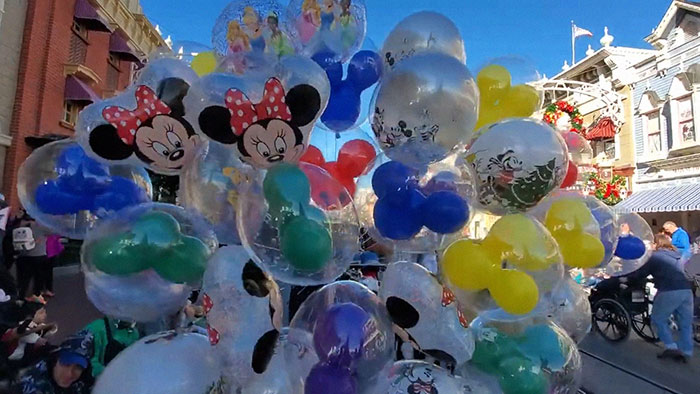 Colorful Disney character balloons including Minnie Mouse and Mickey shapes at a busy theme park on a sunny day, world facts context.