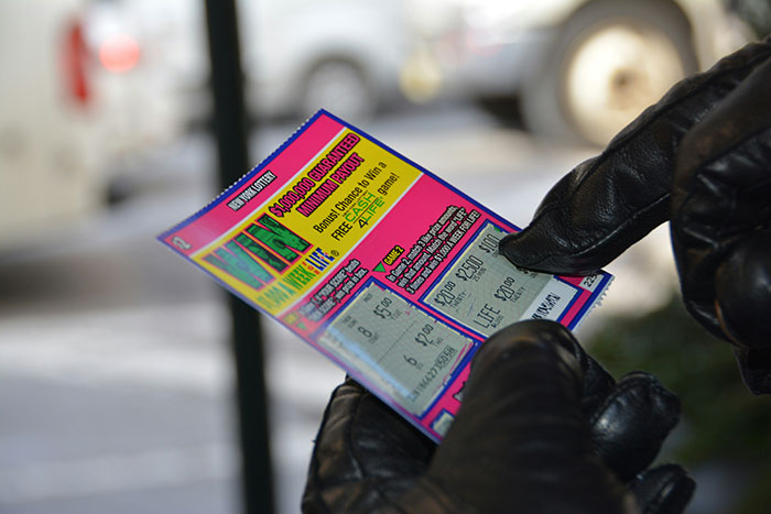 Person wearing black gloves holding a colorful scratch lottery ticket, illustrating cool facts about the world.