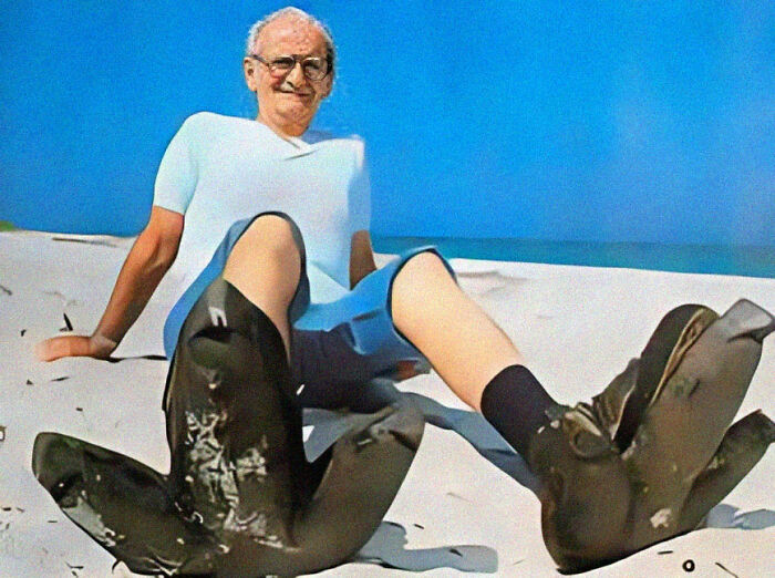 Elderly man sitting on sand wearing oversized boots, illustrating unusual and cool world facts for interest.