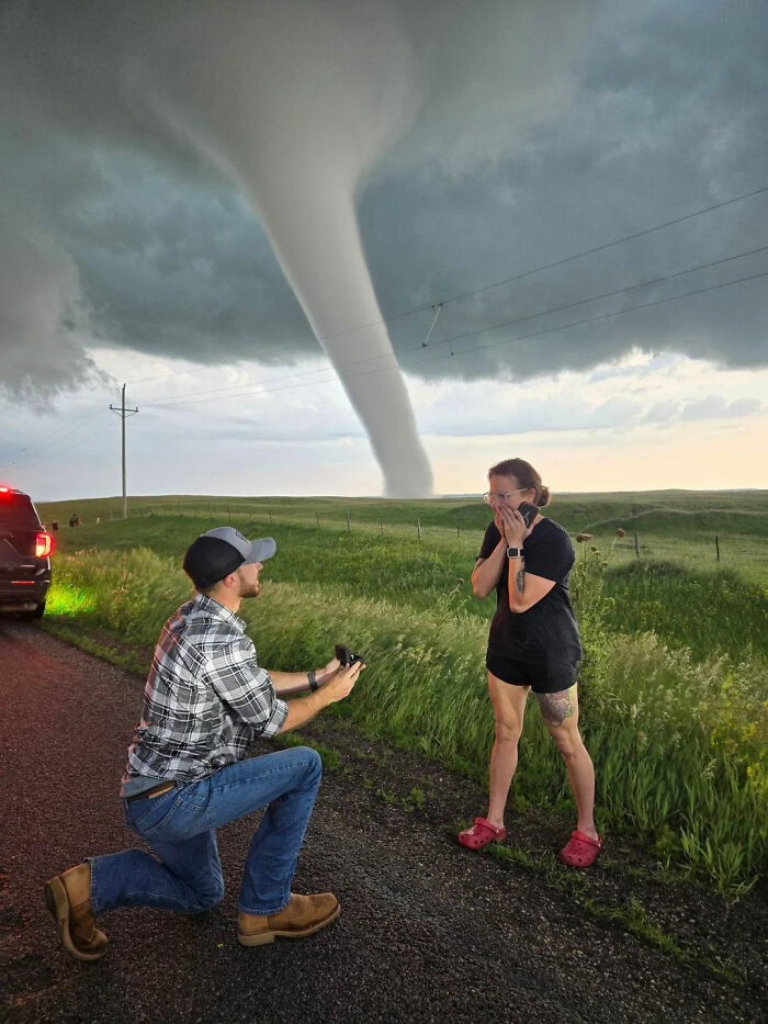 Man proposing to woman on roadside with a large tornado in the background, captured by an online group sharing interesting facts.