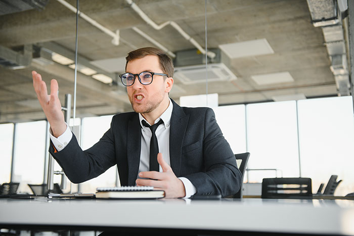 Professional man in a black suit and glasses gesturing passionately during a job interview in a modern office setting.