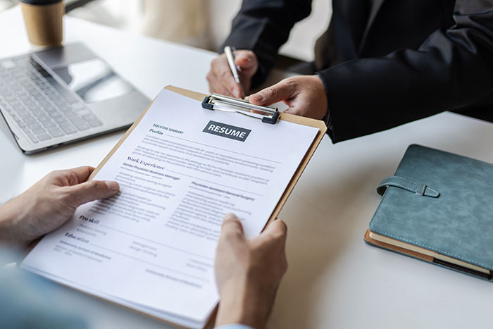 Job interview scene with a candidate holding a resume and an interviewer taking notes before hiring decision.