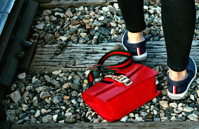 Person wearing navy shoes standing on railway tracks next to a red bag, illustrating bad roommate experiences and awkward situations.