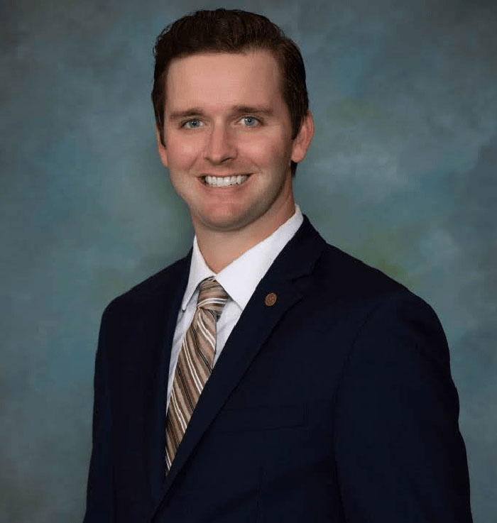 Virginia councilman wearing a dark suit and striped tie, smiling in a formal portrait against a plain background.