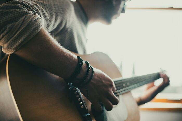 Close-up of a person playing an acoustic guitar indoors, capturing a relaxed moment truckers share craziest things seen - 27