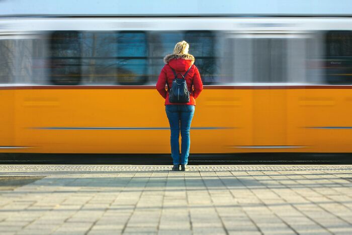 Older person in red jacket standing alone on platform as a yellow train passes by, symbolizing life after divorce. - 26