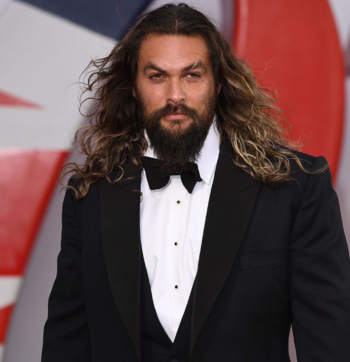 Jason Momoa in a black tuxedo with long hair and beard attending a red carpet event, capturing fans' shocked reaction. - 1
