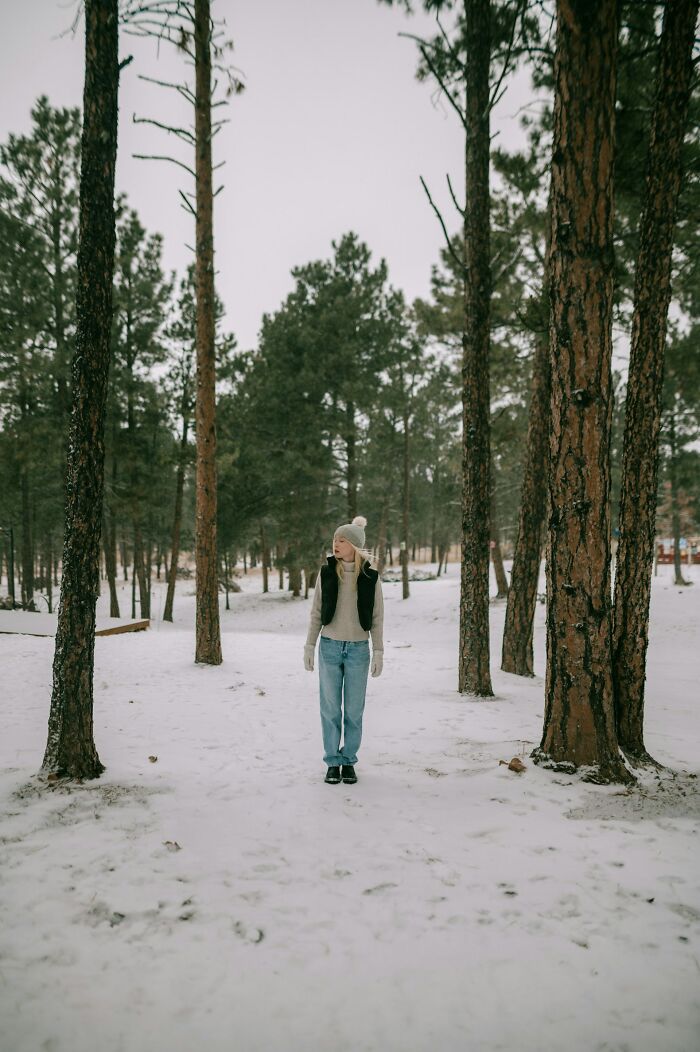 Person standing in snowy forest wearing winter clothes, illustrating survival tips in cold outdoor environments.